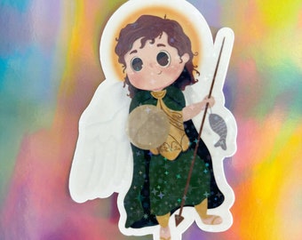 May include: A sticker featuring a cartoon illustration of a winged angel holding a spear and a fish. The angel is wearing a green tunic with gold accents and a halo. The background is a sparkly green with gold stars.