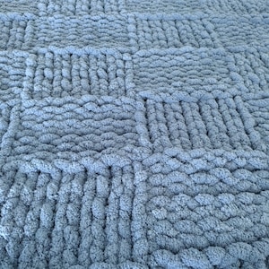 Op de afbeelding: Een close-up van een blauwe gebreide deken met een textuur, geweven patroon.