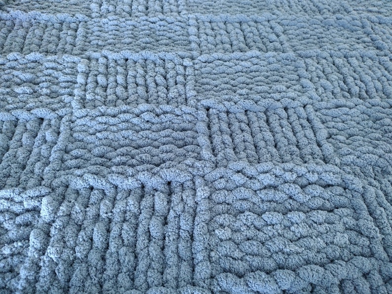 Op de afbeelding: Een close-up van een blauwe gebreide deken met een textuur, geweven patroon.