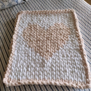 May include: A white and blush pink crocheted baby blanket with a heart design.