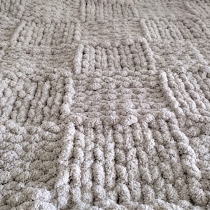 May include: A close-up of a grey chunky knit throw blanket with a textured woven pattern.