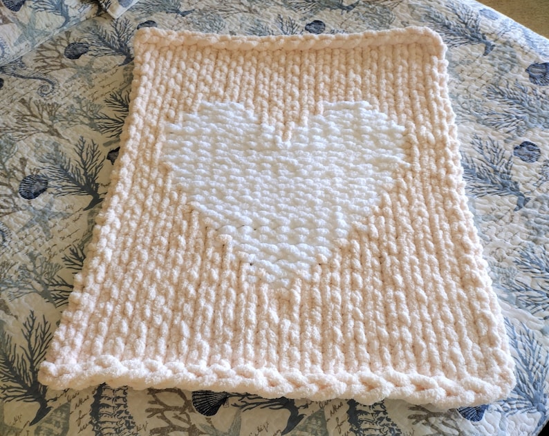 May include: A soft, peach-colored knitted throw blanket with a large white heart in the center.