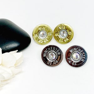 May include: A pair of earrings made from 20 gauge shotgun shells with a clear rhinestone in the center. The shells are gold and silver.