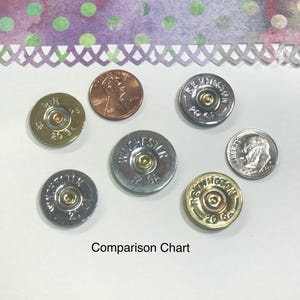 May include: Comparison chart of different shotgun shells and a US penny. The shells are silver, gold, and copper colored. The penny is copper colored. The shells are labeled with the brand name and gauge. The penny is labeled with the year 1999.