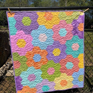 May include: A colorful quilt with a hexagonal pattern in shades of purple, pink, yellow, green, blue, and orange. The quilt is quilted with a wavy design.
