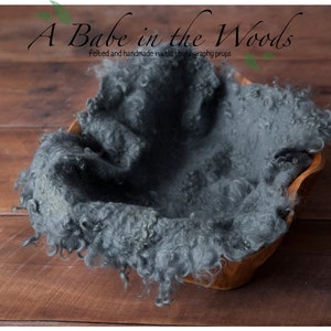 May include: A gray, fluffy, felted newborn photography prop in a wooden bowl. The prop is designed for newborn photography sessions and is made of soft, textured material.