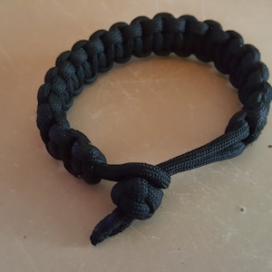 May include: A black paracord bracelet with a knot at the end.