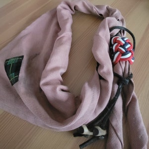 May include: A pink scarf with a black and white plaid patch and a red, white, and blue knotted cord.