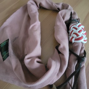 May include: A pink fabric scarf with a black cord and a red and white braided cord tied around a wooden stick.