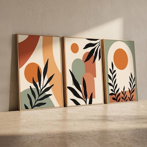 Puede incluir: Conjunto de tres láminas artísticas enmarcadas con diseños abstractos. Cada lámina presenta un fondo beige con formas naranjas, verdes y melocotón, y siluetas de hojas negras. Los marcos son de madera clara, de estilo moderno y minimalista.