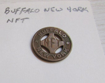 Może przedstawiać: Dwa zabytkowe metalowe żetony. Pierwszy żeton jest srebrny i zawiera napis "INT. RY. CO. BUFFALO". Drugi żeton jest brązowy i zawiera napis "BUFFALO NEW YORK NFT".