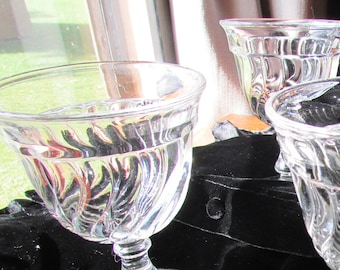 May include: Four clear glass goblets with a swirl design on a black velvet surface.