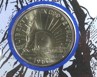 Może przedstawiać: Srebrna moneta kolekcjonerska o nominale 50 centów przedstawiająca Statuę Wolności z napisem "Liberty", "In God We Trust" i "1986".