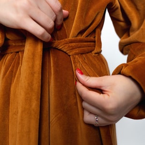 May include: A brown velvet robe with a self-tie belt. The robe is tied at the waist and the sleeves are long.