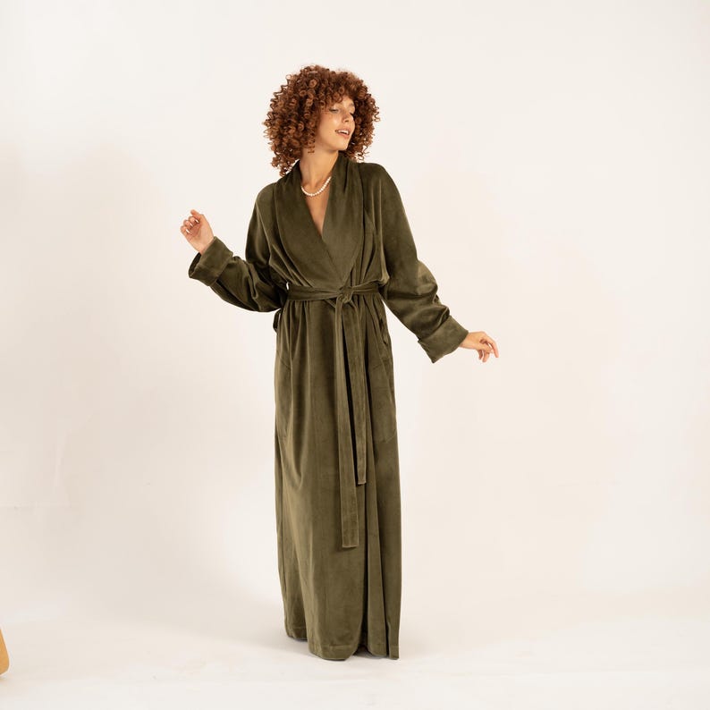 May include: An olive green robe with a wrap-around design and a matching belt. The long-sleeved robe has a soft, velvety texture and a relaxed fit. The robe is floor-length and features pockets.