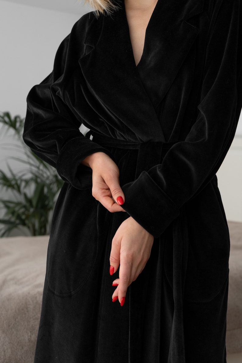 May include: A black velvet robe with a shawl collar and a tie belt. The robe has long sleeves and two pockets.