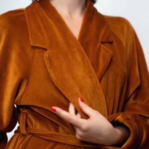 May include: A long, brown velvet robe with a shawl collar and a tie belt. The robe is worn by a person with red nail polish.