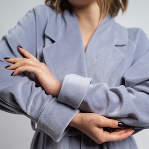 Peut inclure: Une robe douce de couleur bleu clair avec un col châle et des manches longues. La robe est en velours et possède une ceinture à nouer.