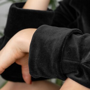May include: Close-up of a black velvet sleeve with a folded cuff. The fabric is soft and textured.