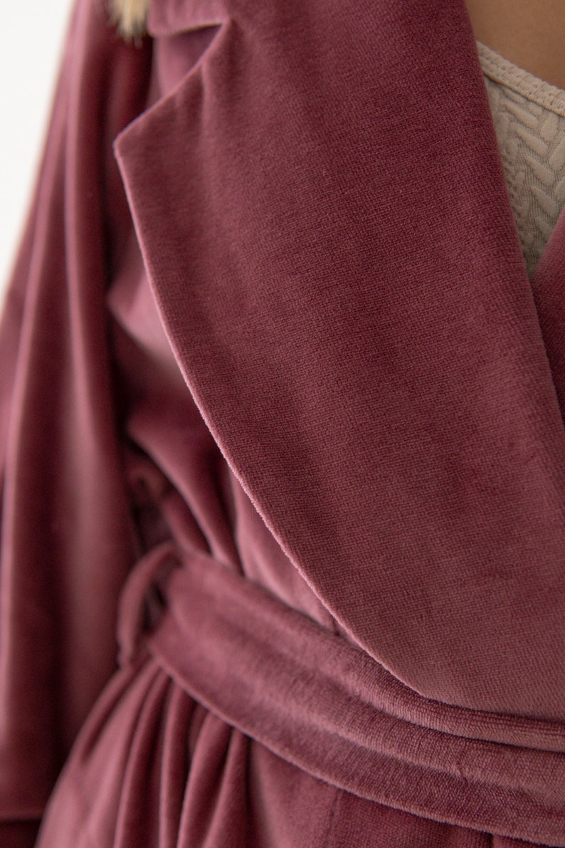 Puede incluir: Una bata de terciopelo rosa polvoriento con una cinta para atar. La bata tiene un cuello chal y mangas largas.