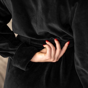 May include: A black velvet robe with a tie belt. The robe is worn by a person with red nail polish.