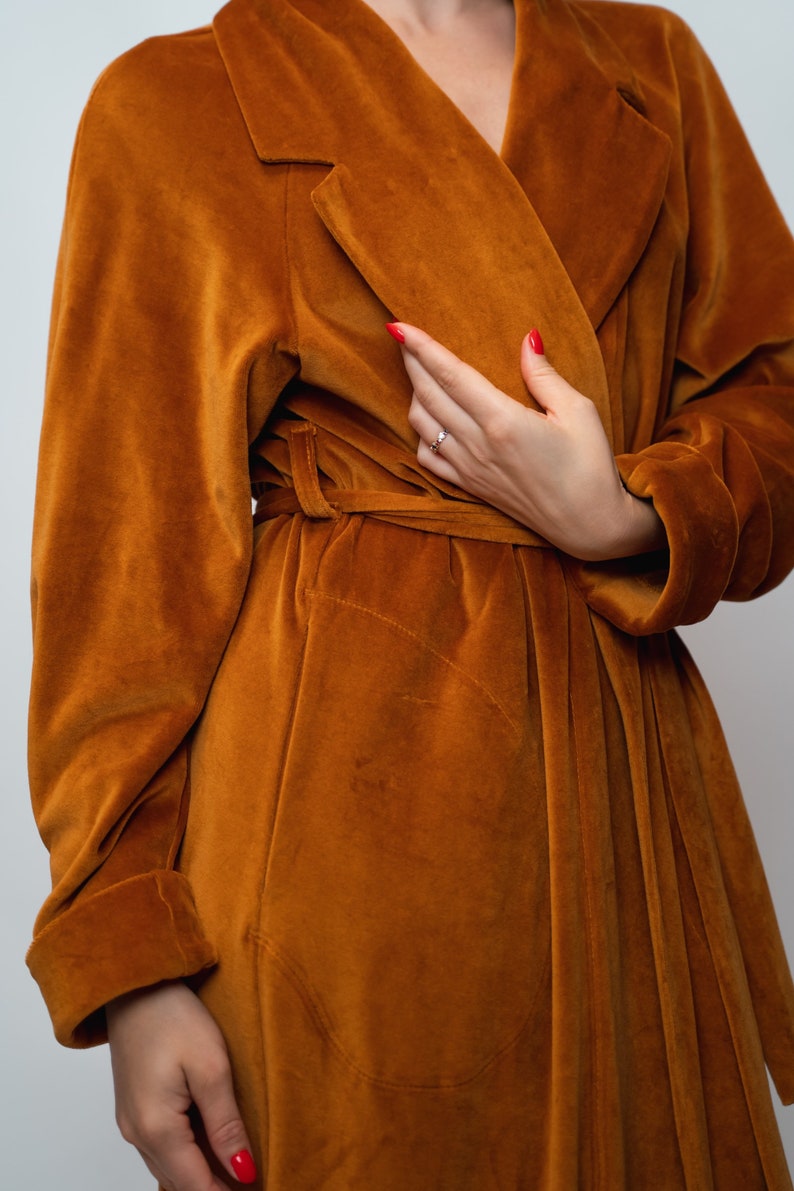 May include: A long-sleeved, rust-colored velvet robe with a self-tie belt. The robe has a shawl collar and a relaxed fit.