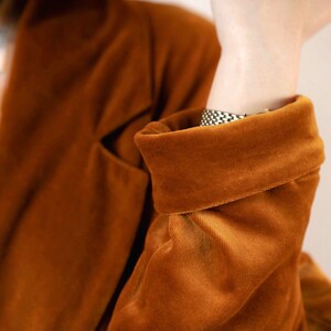 May include: A close-up of a brown velvet blazer with a folded cuff. The blazer has a soft, plush texture.