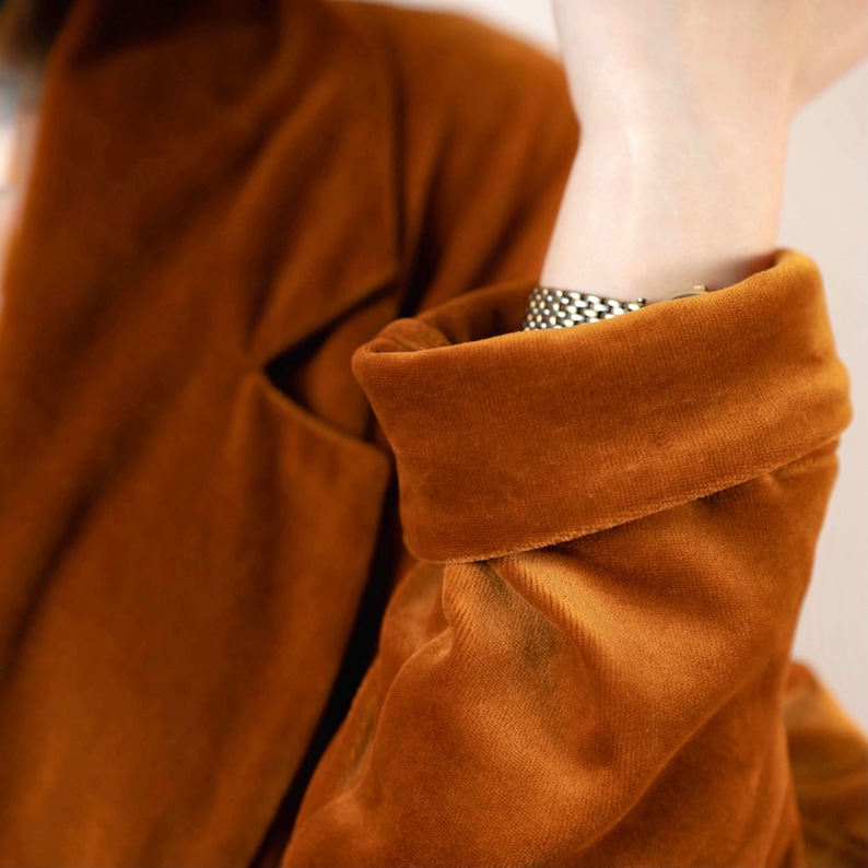 May include: A close-up of a brown velvet blazer with a folded cuff. The blazer has a soft, plush texture.