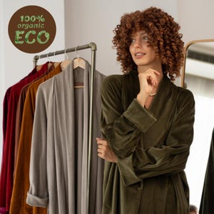 May include: A woman in a dark green velvet robe. A clothes rail displays robes in shades of red, brown, and grey. The image features a circular logo with the words "100% organic ECO".