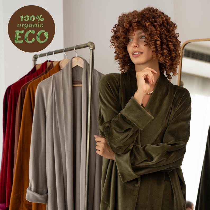 May include: A woman in a dark green velvet robe. A clothes rail displays robes in shades of red, brown, and grey. The image features a circular logo with the words "100% organic ECO".