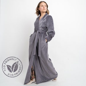 May include: A long, gray robe with a shawl collar and a tie belt. The robe has pockets on the sides and a long slit in the front. The robe is made of a soft, plush fabric. The label on the robe says "ECO FRIENDLY".