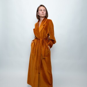 May include: A long, rust-colored velvet robe with a shawl collar and a tie belt.