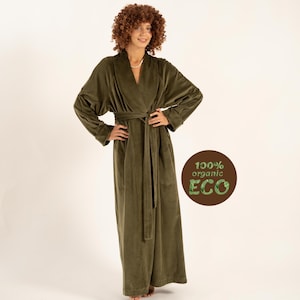 May include: An olive green robe with a shawl collar and a matching belt. The long, plush robe is made of a soft material and has long sleeves. The image also includes a circular graphic with the text "100% organic ECO".