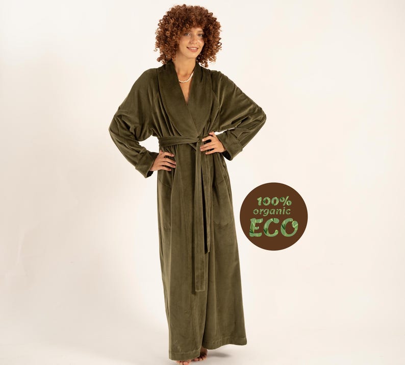 May include: An olive green robe with a shawl collar and a matching belt. The long, plush robe is made of a soft material and has long sleeves. The image also includes a circular graphic with the text "100% organic ECO".