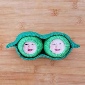 Può includere: Due baccelli di piselli all'uncinetto con facce di bambino all'interno. I baccelli di piselli sono verdi e le facce sorridono.