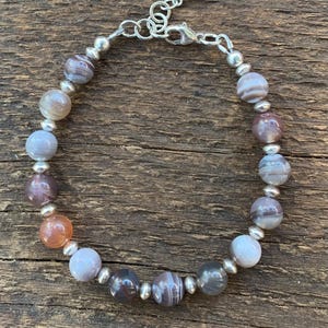 May include: A silver bracelet with a clasp closure and a row of round, gray, white, and orange agate beads.