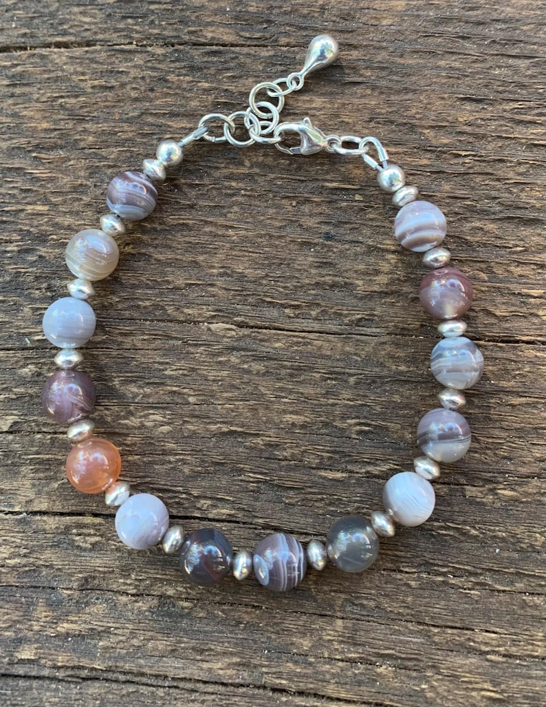 May include: A silver bracelet with a clasp closure and a row of round, gray, white, and orange agate beads.
