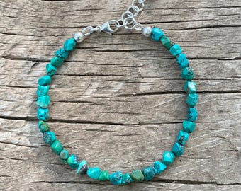 May include: A turquoise gemstone bracelet with a silver clasp. The bracelet is made of small, irregular shaped turquoise stones.