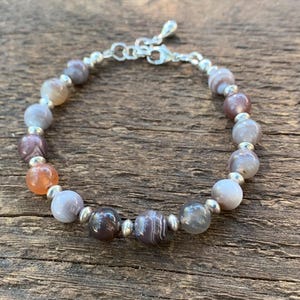 May include: A bracelet made with silver and agate beads. The beads are a mix of gray, brown, and orange colors.