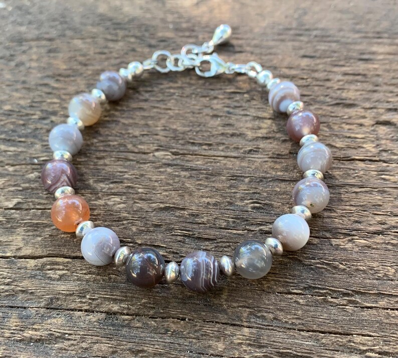May include: A bracelet made with silver and agate beads. The beads are a mix of gray, brown, and orange colors.