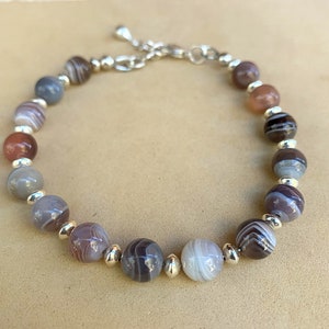 May include: A bracelet made with brown, gray, and white agate beads and silver spacers.