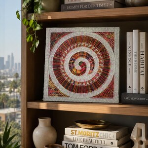 May include: A square wall art piece featuring a central spiral design composed of multicolored vertical threads, surrounded by a white textured border with a repeating circular pattern, set against a background of various books on wooden shelves.