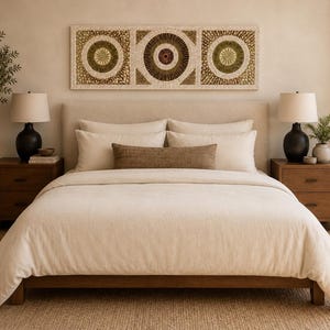 May include: A bedroom set featuring a low-profile wooden bed frame with a cream-colored duvet, two matching square pillows, and a rectangular brown lumbar pillow. Two wooden nightstands with black lamps flank the bed, topped by wall art.