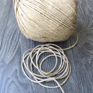 Könnte beinhalten: Eine Kugel aus Naturbast mit einem losen Ende, die sich auf einer dunklen Holzoberfläche abwickelt.