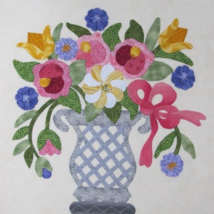 May include: A blue and white ceramic vase with a lattice design holds a bouquet of colorful flowers. The flowers include pink, yellow, red, and white blooms. The vase is sitting on a white background.