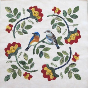 Può includere: Un tessuto bianco con un disegno floreale con rose rosse con centri gialli e foglie verdi. Due uccelli blu sono appollaiati su un ramo con foglie verdi.