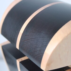 May include: A wooden box with a black and natural wood finish. The box has a curved top and a black stripe around the edge.