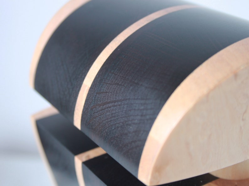 May include: A wooden box with a black and natural wood finish. The box has a curved top and a black stripe around the edge.