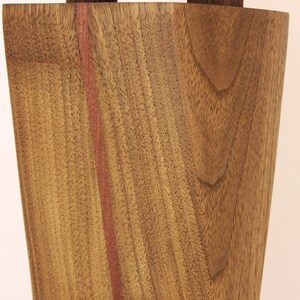 K&ouml;nnte beinhalten: Nahaufnahme einer Holzvase mit einem rotbraunen Streifen in der Mitte. Die Holzmaserung ist sichtbar und die Vase hat eine leicht geschwungene Form.