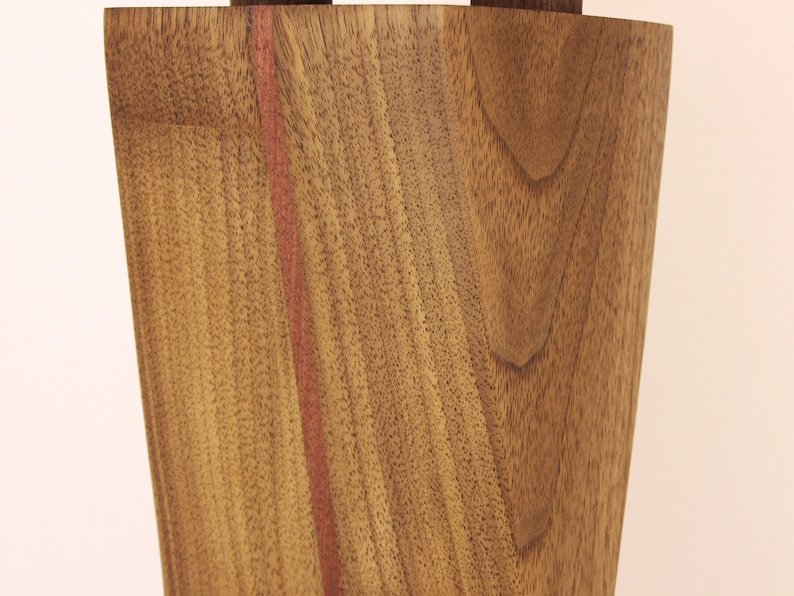 K&ouml;nnte beinhalten: Nahaufnahme einer Holzvase mit einem rotbraunen Streifen in der Mitte. Die Holzmaserung ist sichtbar und die Vase hat eine leicht geschwungene Form.